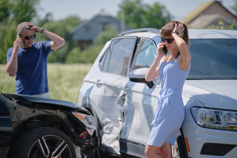 Angry woman and man drivers of heavily damaged vehicles calling insurance service for help in car crash accident on street side. Road safety concept.