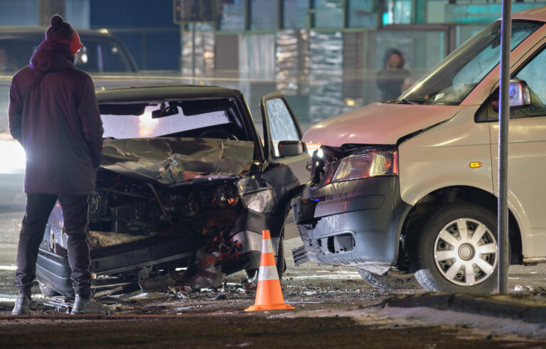 Cars crashed heavily in road accident after collision and silhouette of people on city street at night. Road safety and insurance concept.